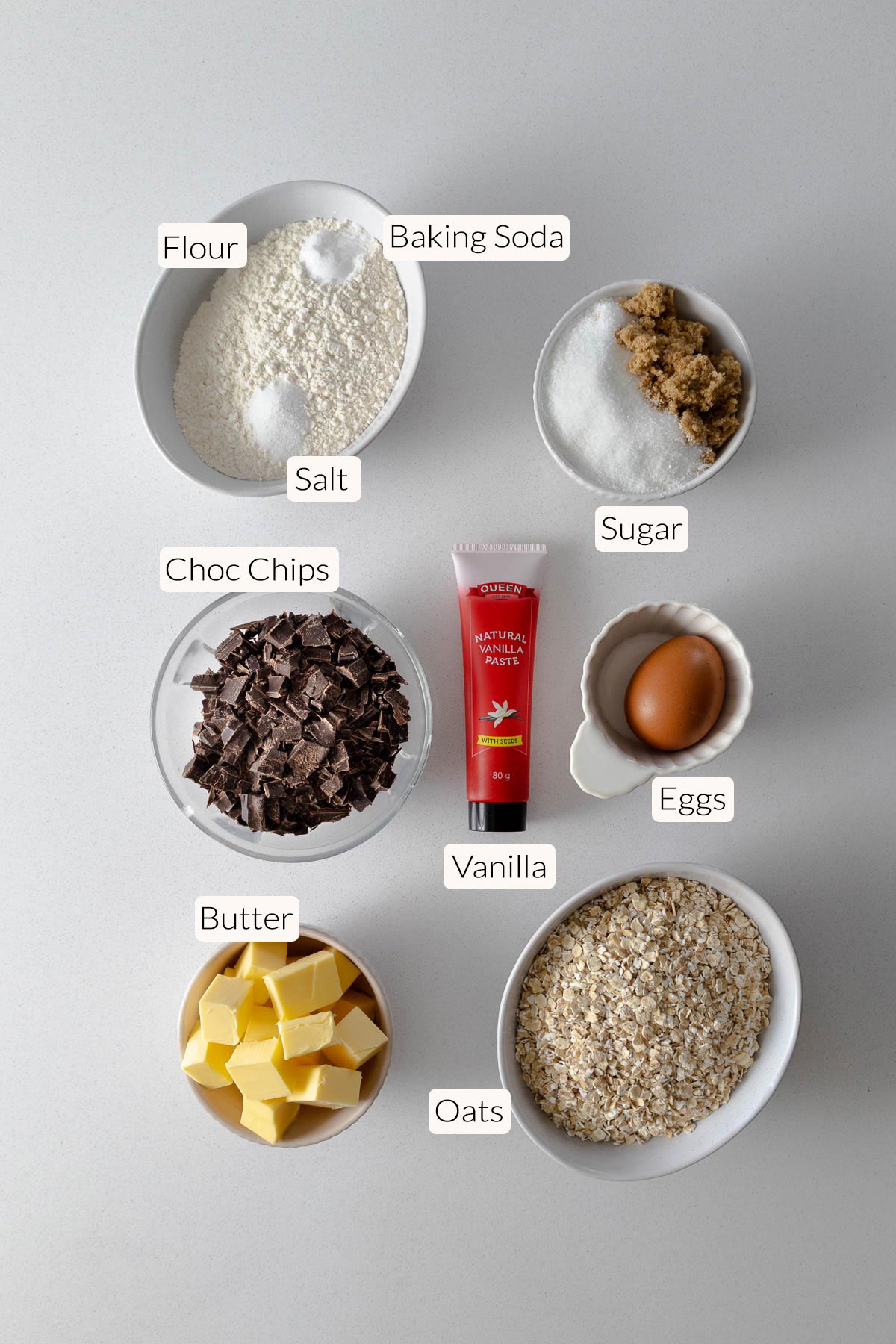 Oatmeal chocolate chip cookie ingredients - flour, baking soda, salt, sugar, chocolate chips, vanilla, eggs, butter, and oats.